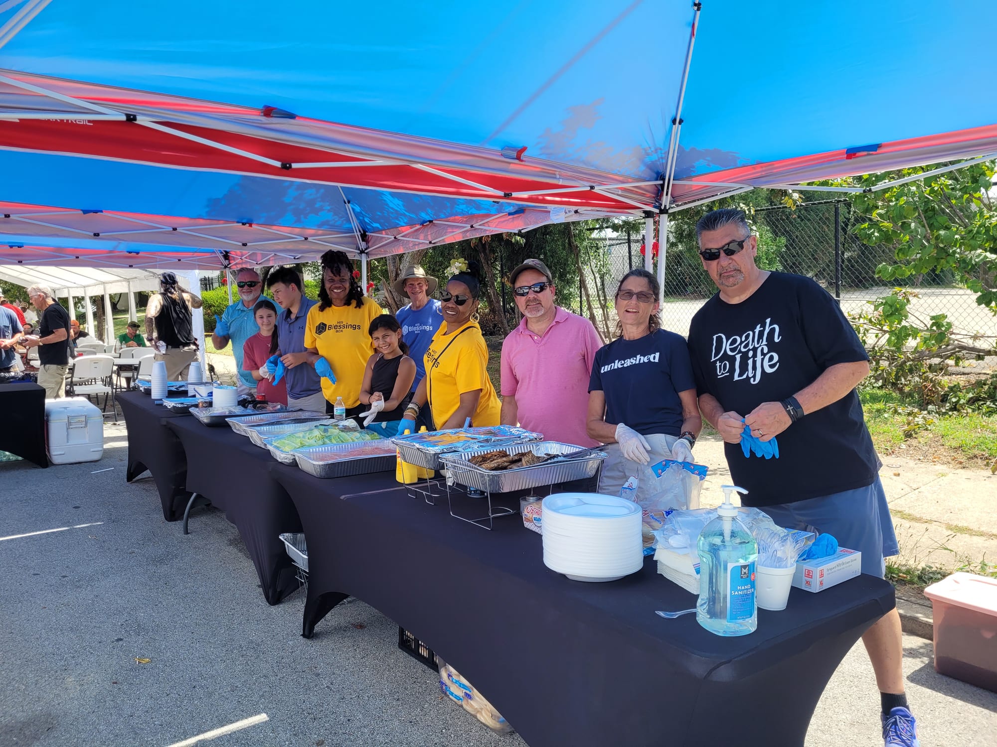 His Blessings Box volunteers serving trays of food under red and blue tents at a Louisville community day