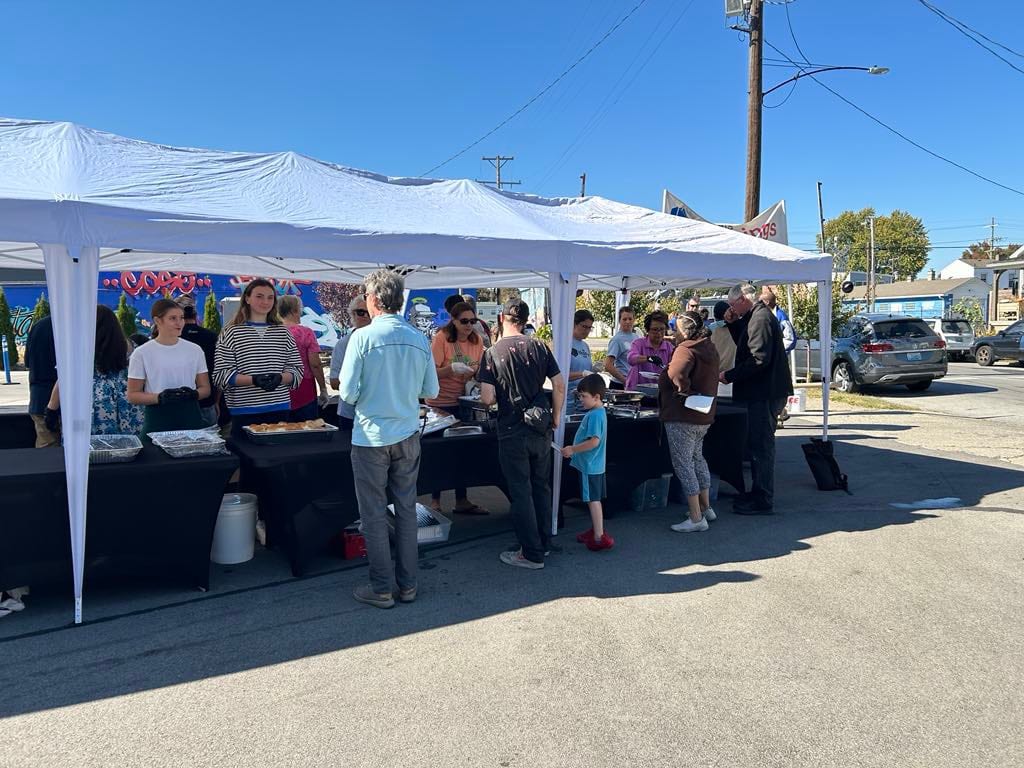 Guests and volunteers along serving tables under white canopies in the Mary Street lot