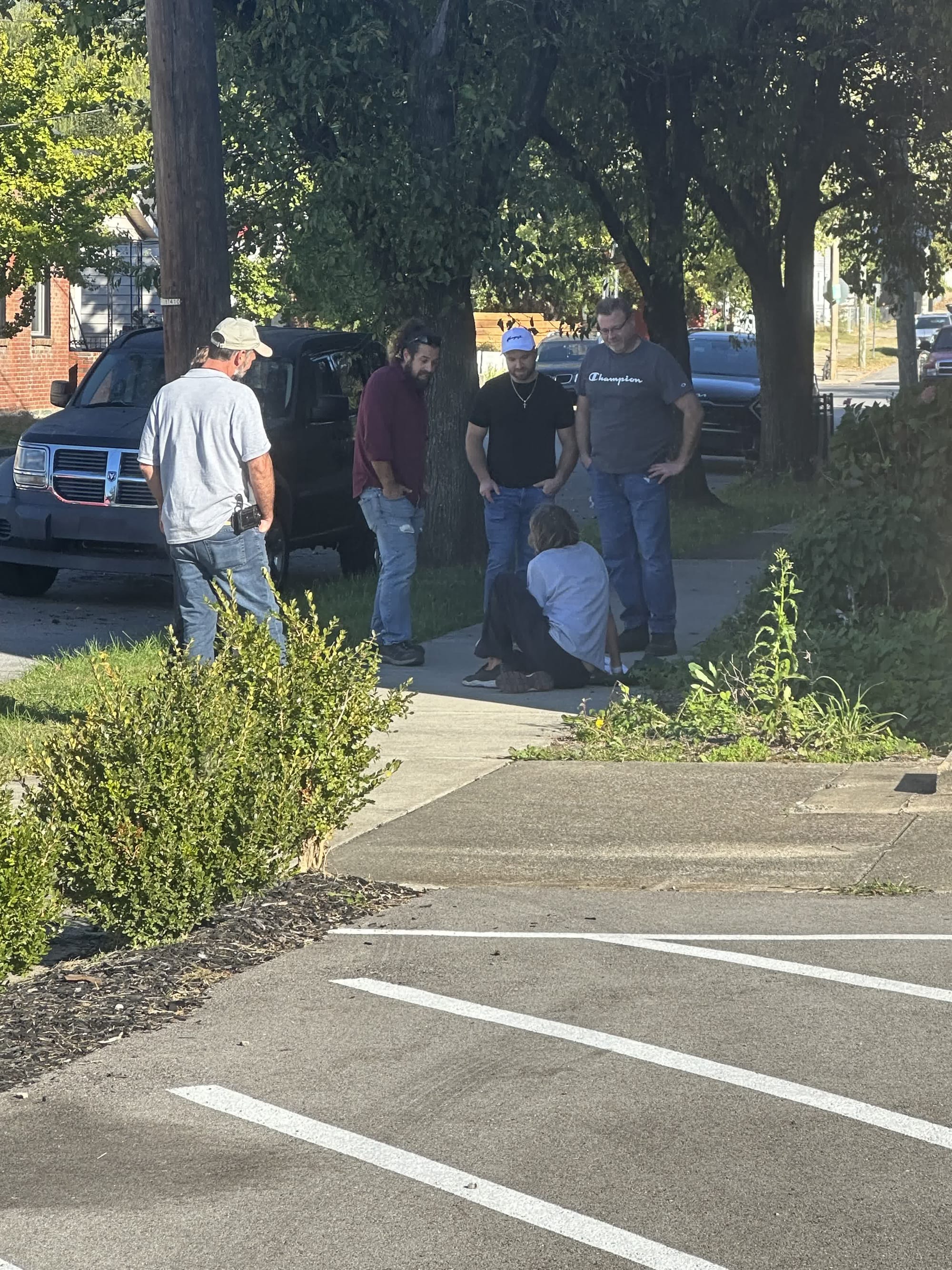 Four volunteers standing on the sidewalk talking with a neighbor sitting on the curb